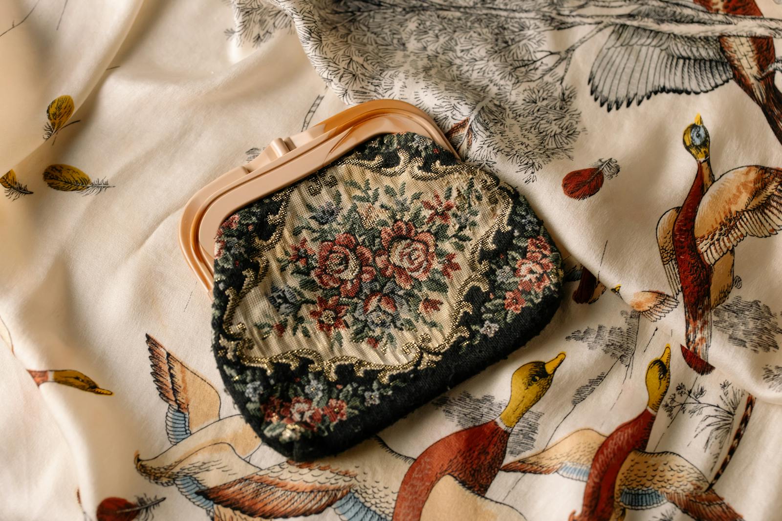 A vintage floral clutch bag resting on a patterned fabric with bird illustrations.