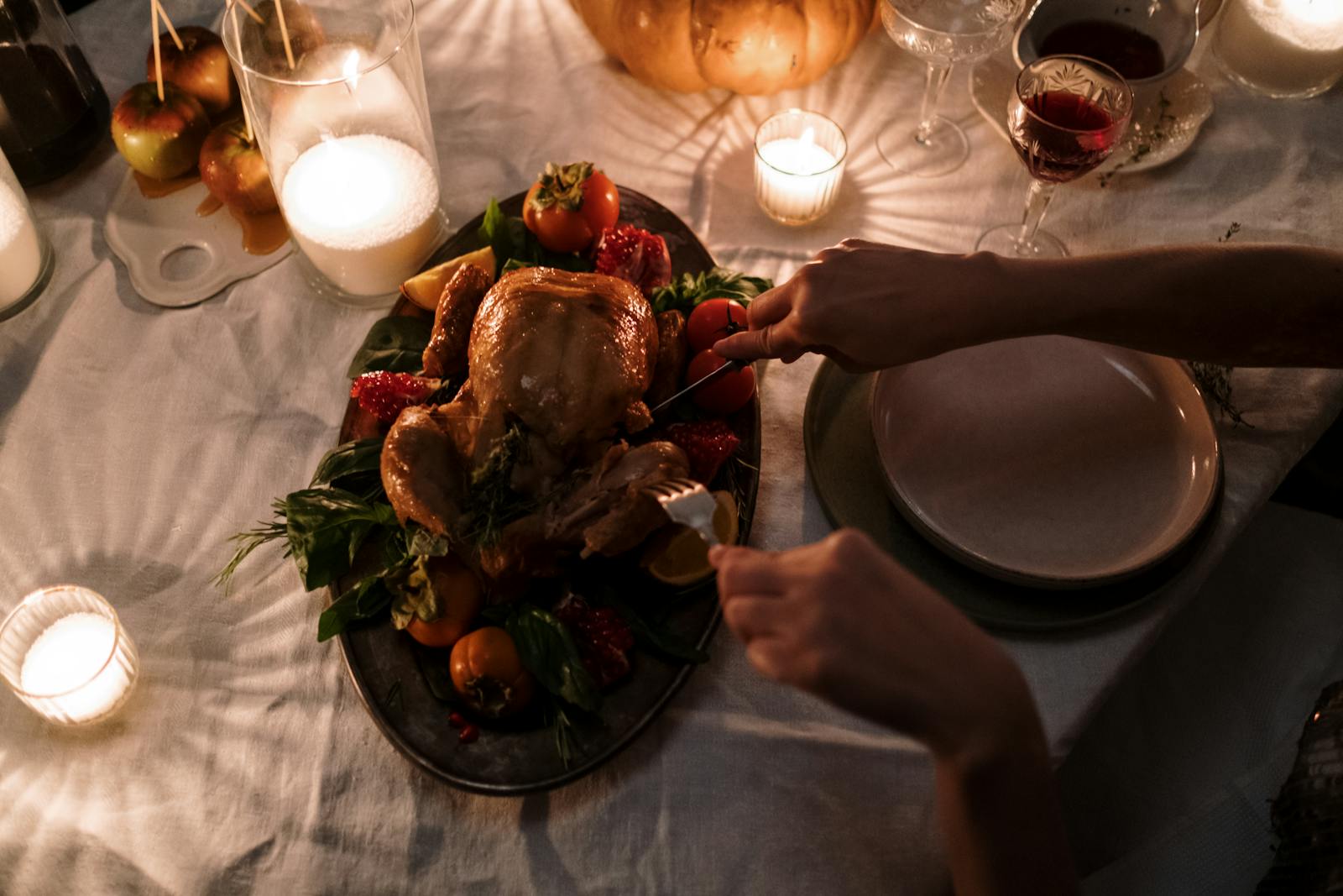 A warm holiday dinner setting featuring a roast turkey being sliced on a candlelit table.