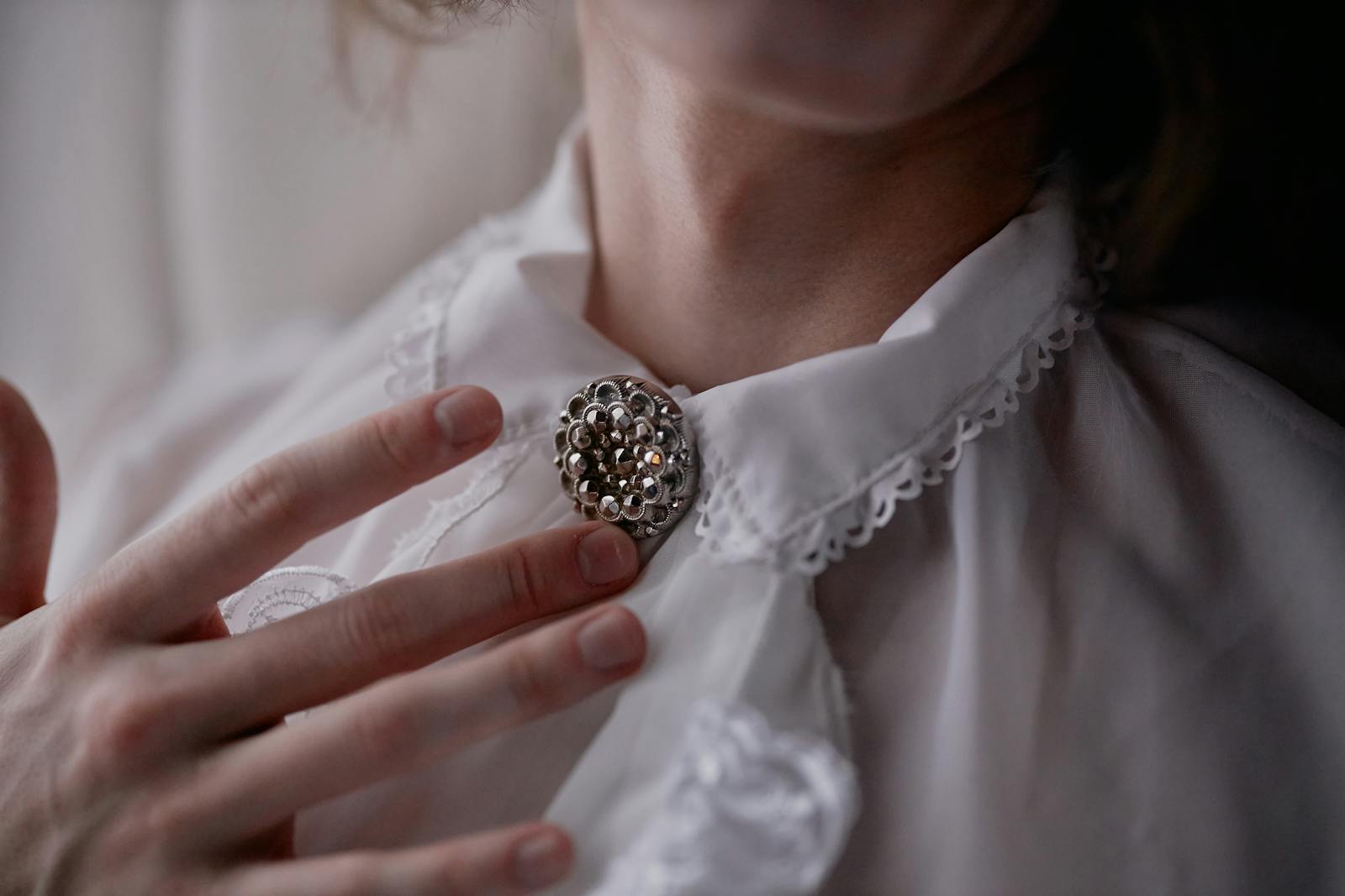 Close-up of an elegant vintage brooch pinned on a lace collar, with soft hands gently touching.