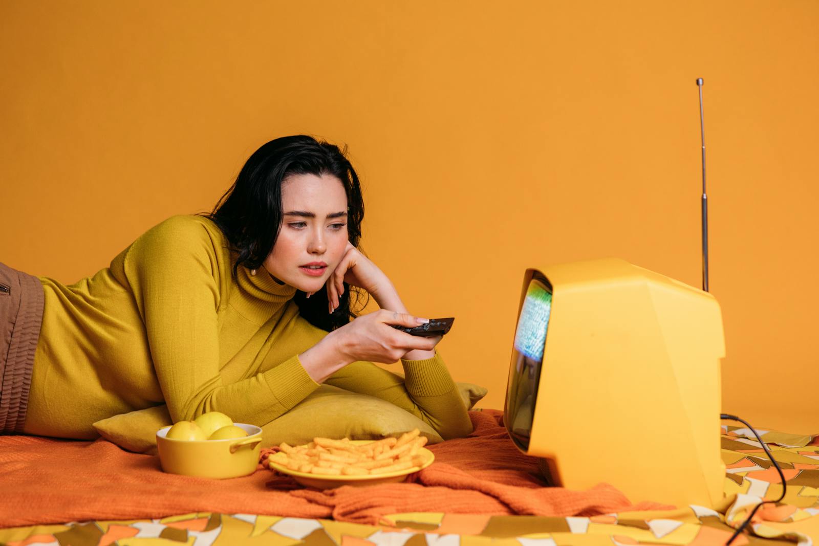 Woman relaxing and watching a vintage television set while snacking on yellow chips.