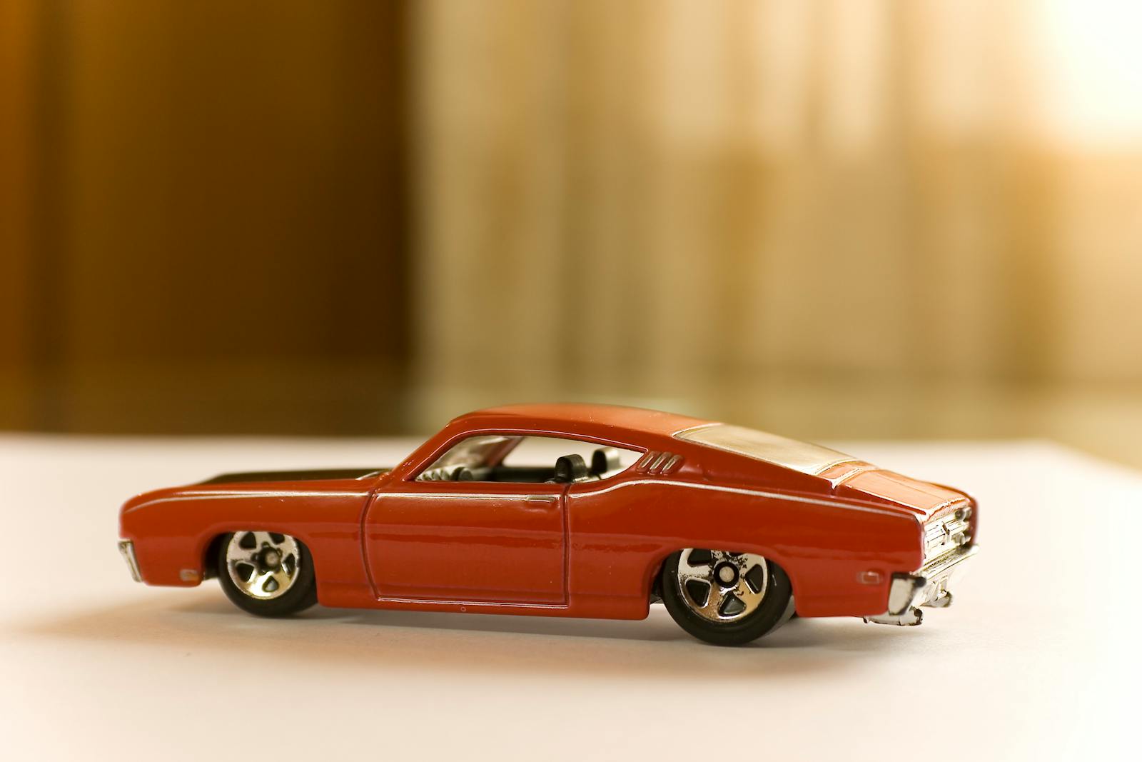 Close-up of a red vintage toy car on a white surface indoors.