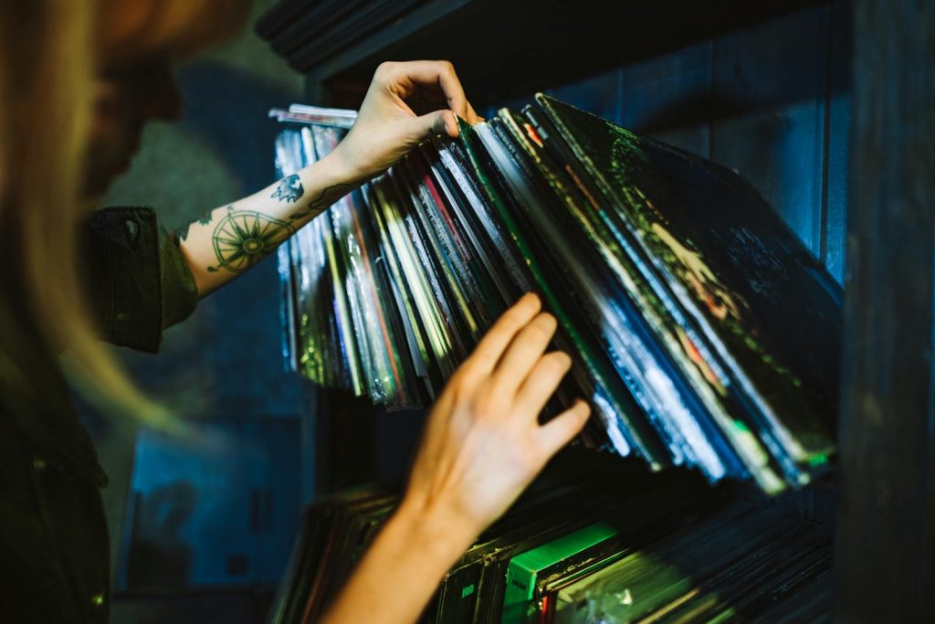 Close-up of a woman picking vinyl records from a shelf with a tattooed arm.