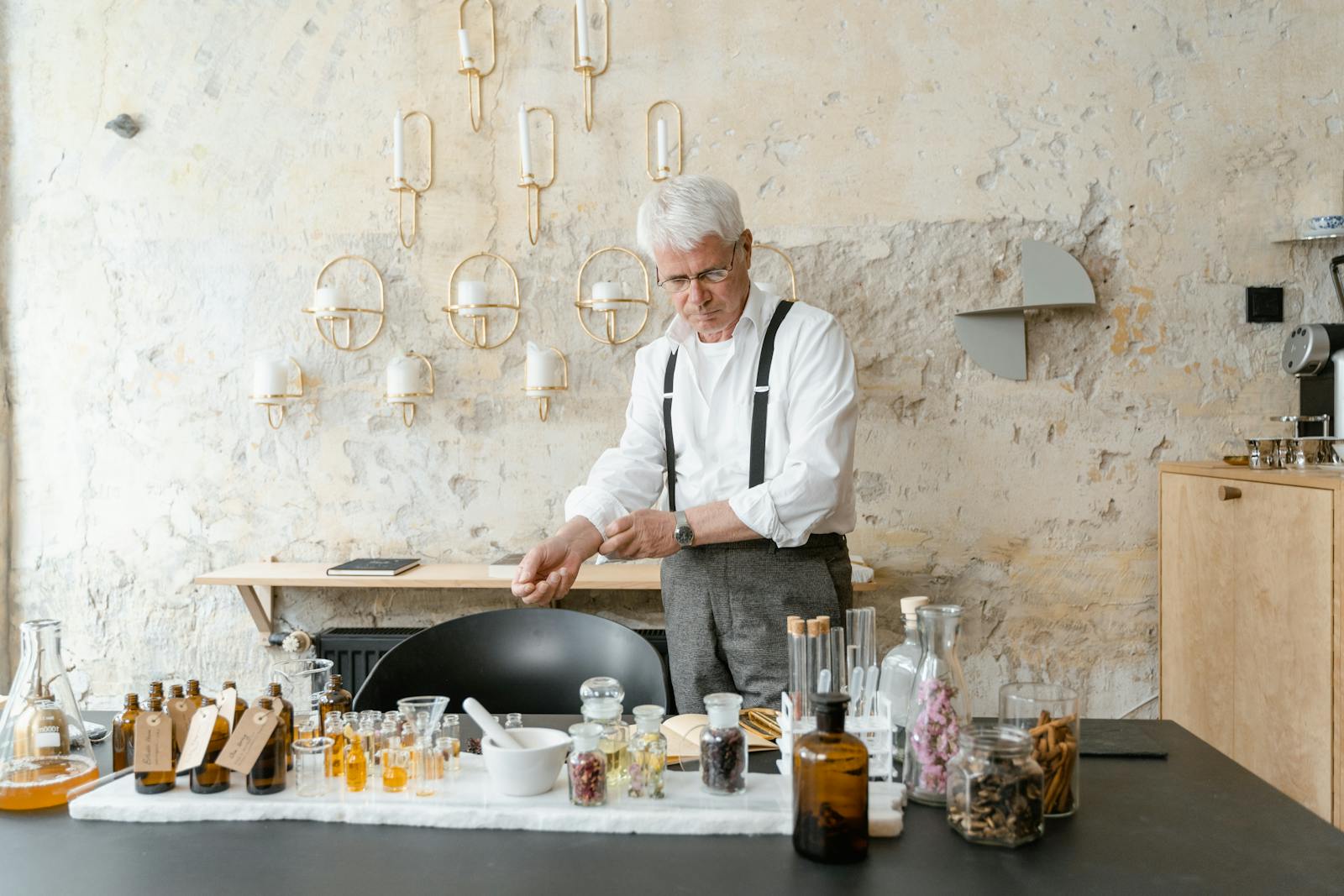 Senior man blending natural fragrances in a rustic setting with bottles and dried flowers.