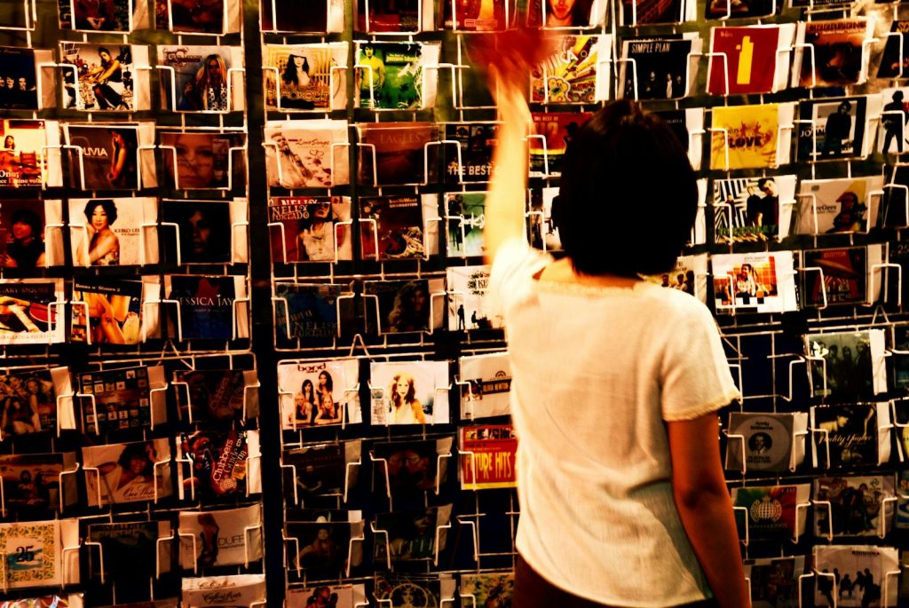 A person browsing various CDs in a music store, reaching for a disc on a shelf.