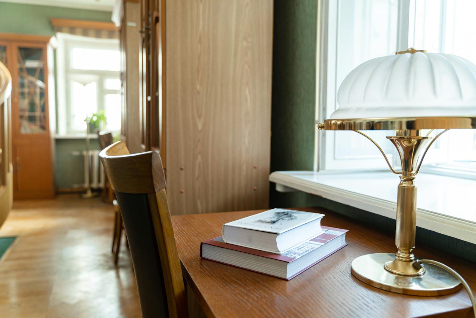 A cozy study area with books stacked beside a classic desk lamp in a softly lit room.