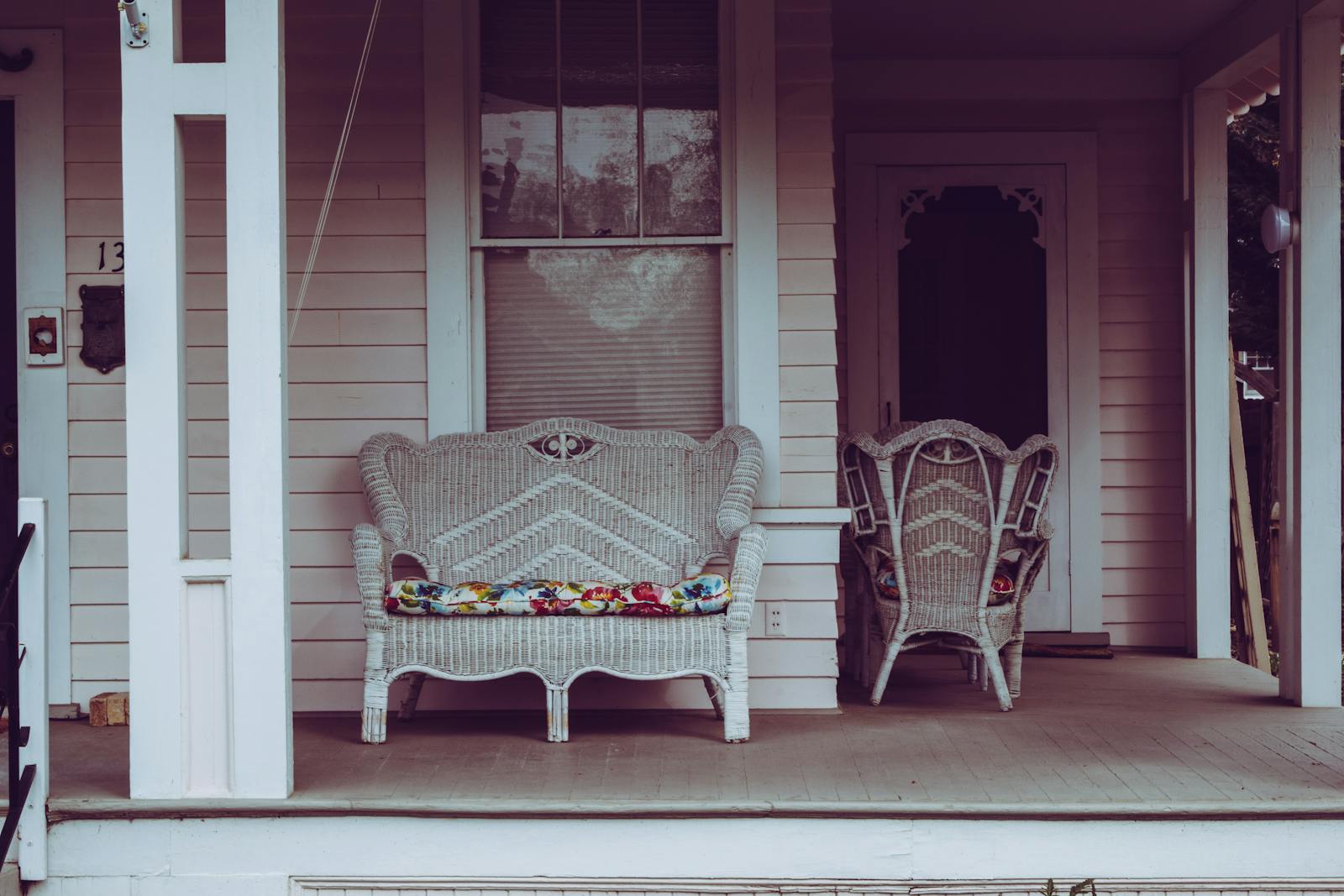 Cozy vintage-style front porch with white wicker chairs and floral cushions.
