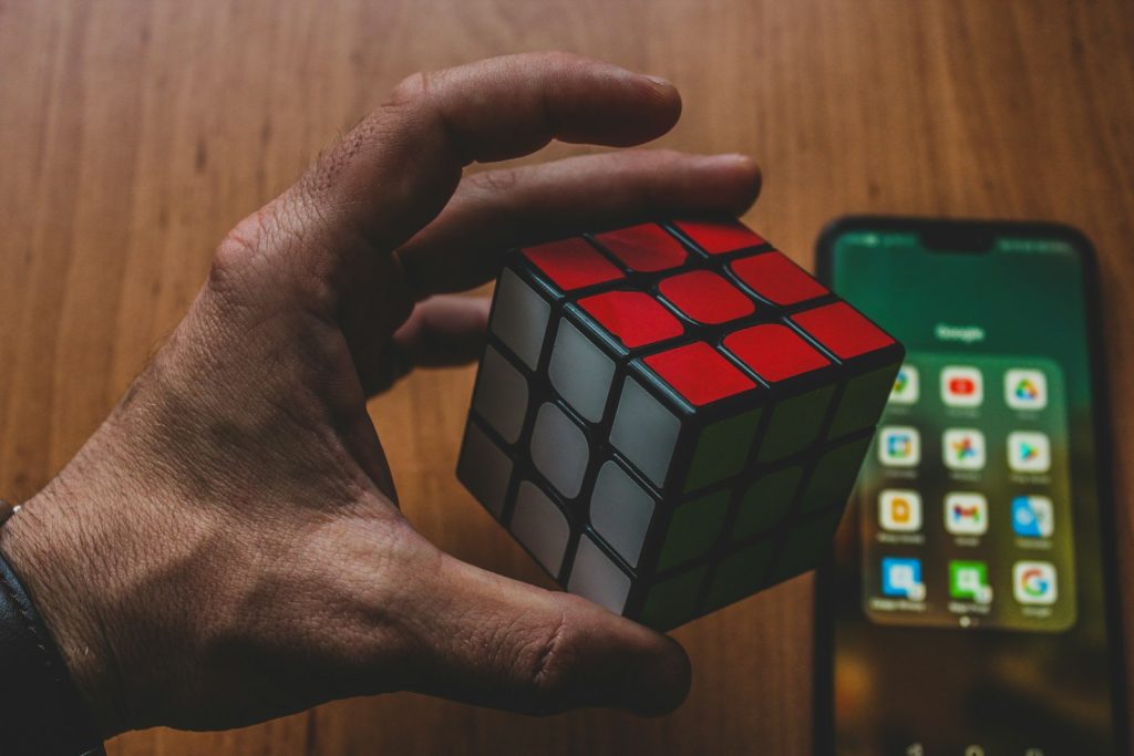 a hand holding a rubik cube next to a cell phone