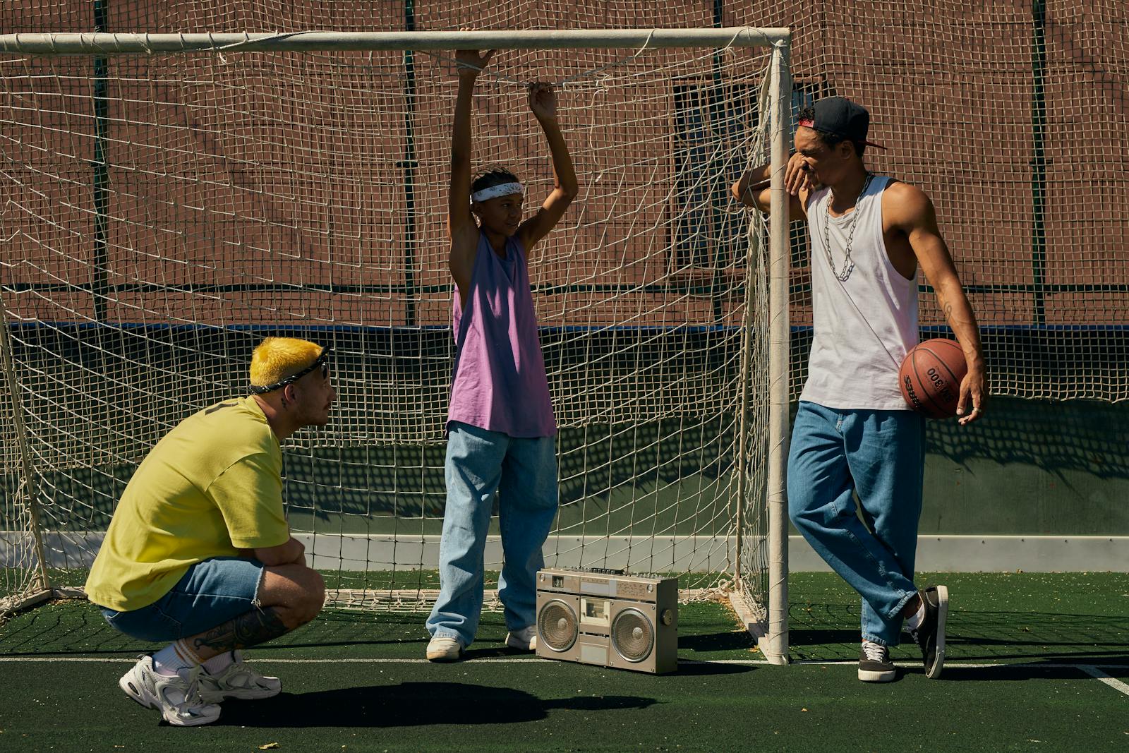 Three young men relaxing on a sports ground with a basketball and boombox.
