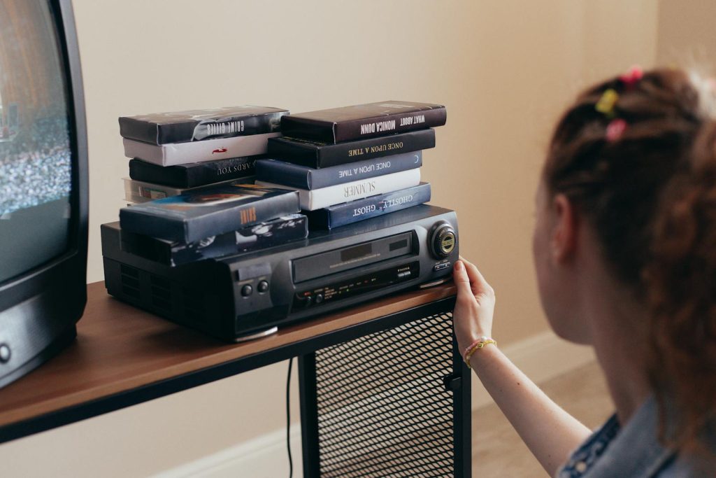Young woman engaging with retro VHS tapes and a classic VCR setup.