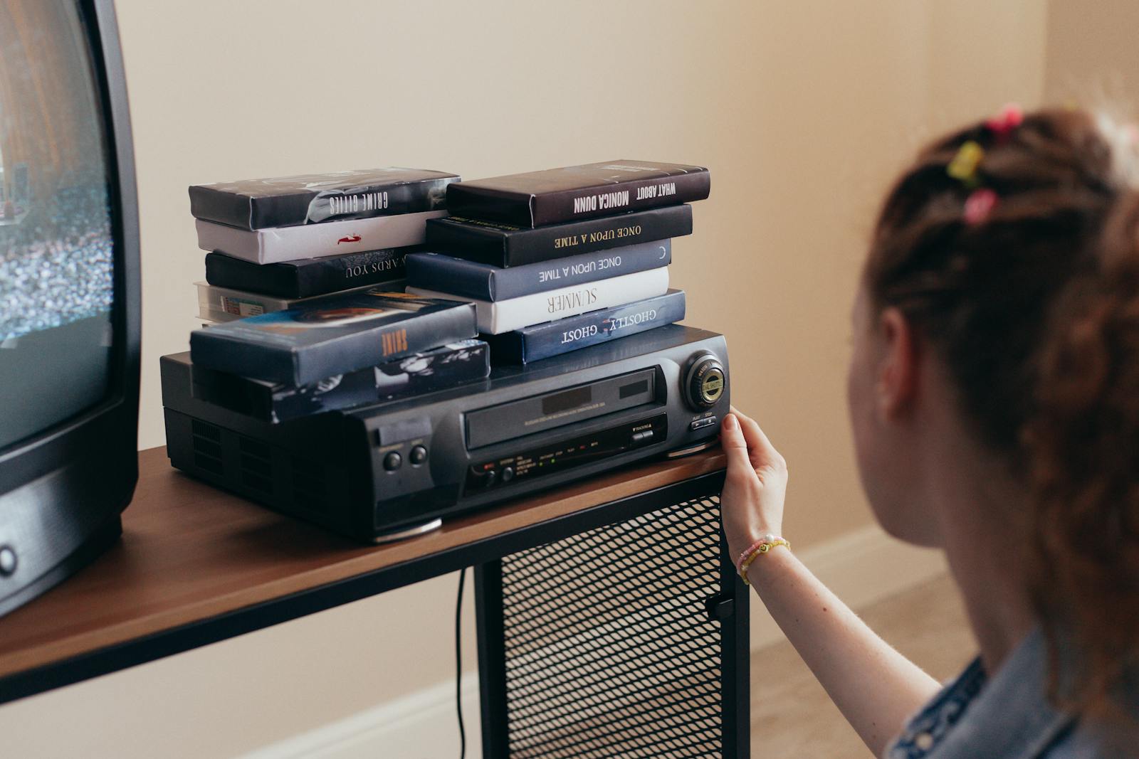 Young woman engaging with retro VHS tapes and a classic VCR setup.