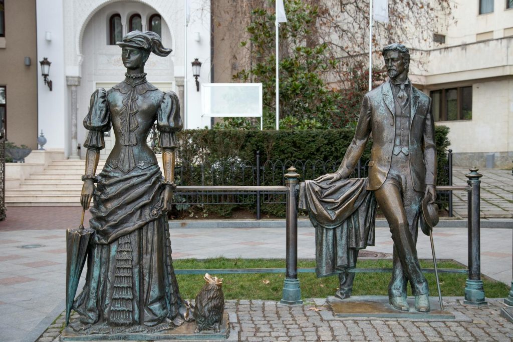 Two Victorian-era bronze statues outdoors in a city setting, capturing timeless elegance.