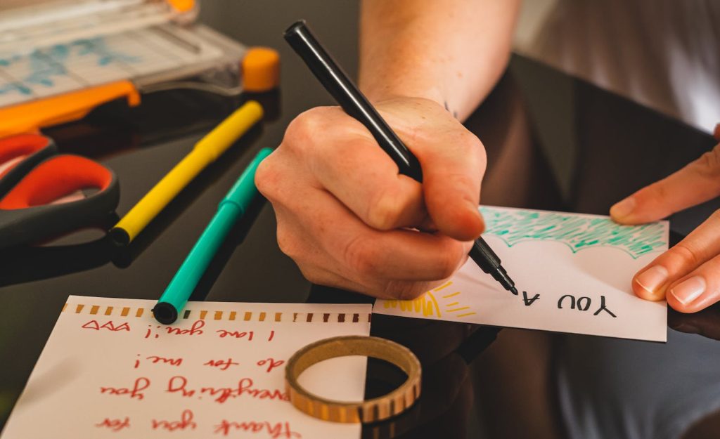 Close-up of a person creatively writing on colorful paper with various art materials around.