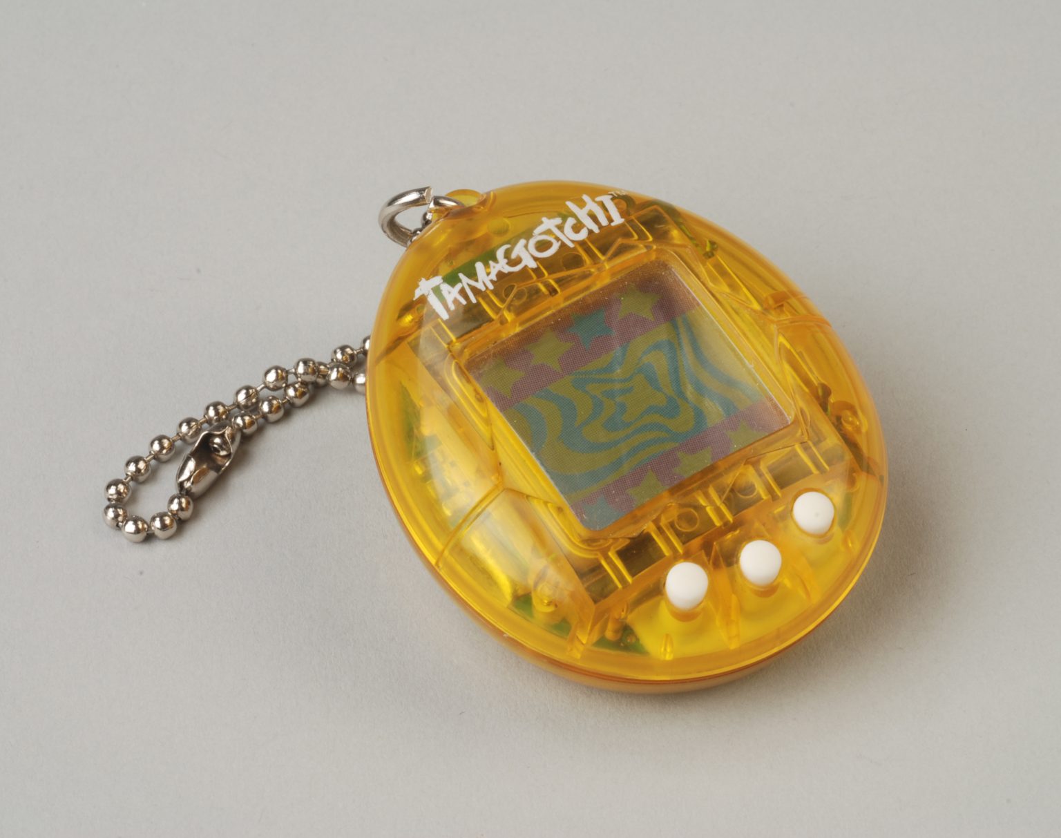 Close-up of a classic yellow Tamagotchi virtual pet keychain toy from the original 1990s design