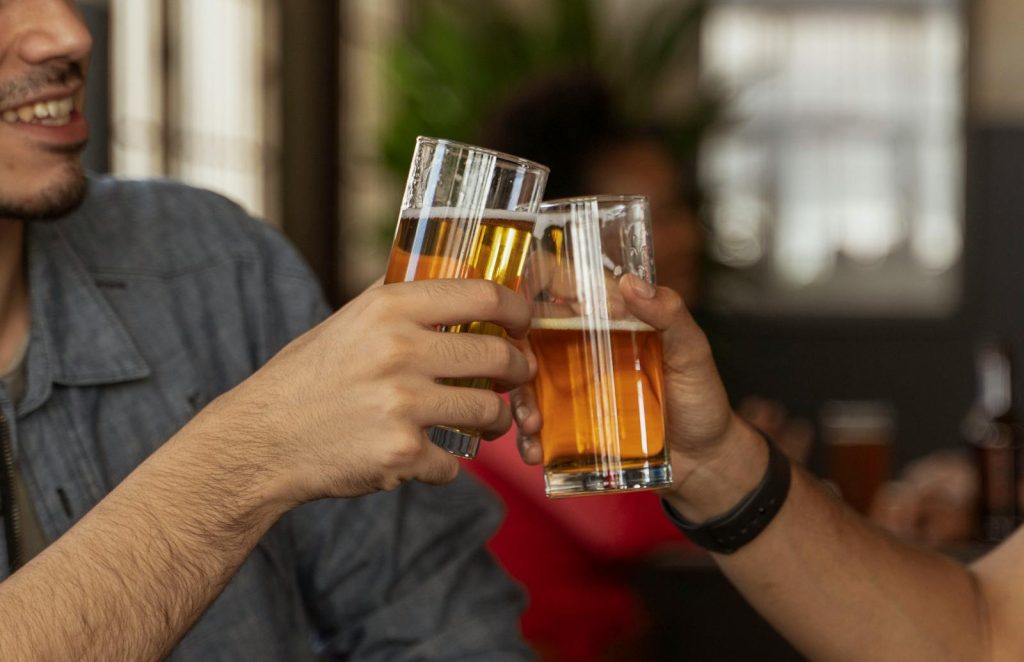 Two people clinking glasses of beer, celebrating in a casual indoor setting.