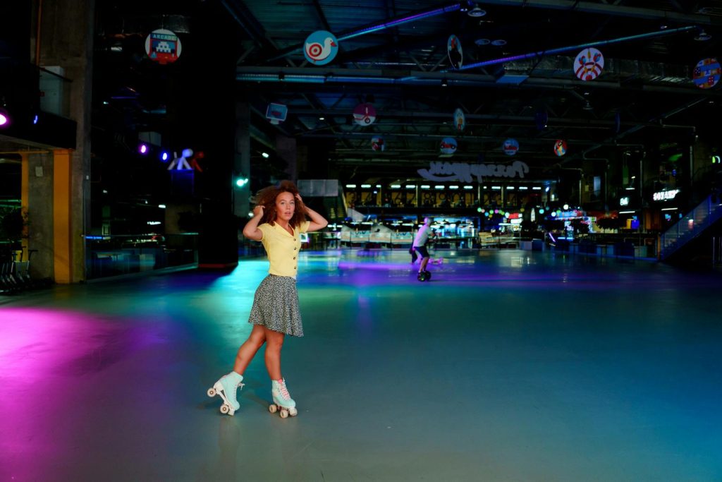 Woman in yellow top roller skating in a neon-lit indoor rink, vibrant atmosphere.