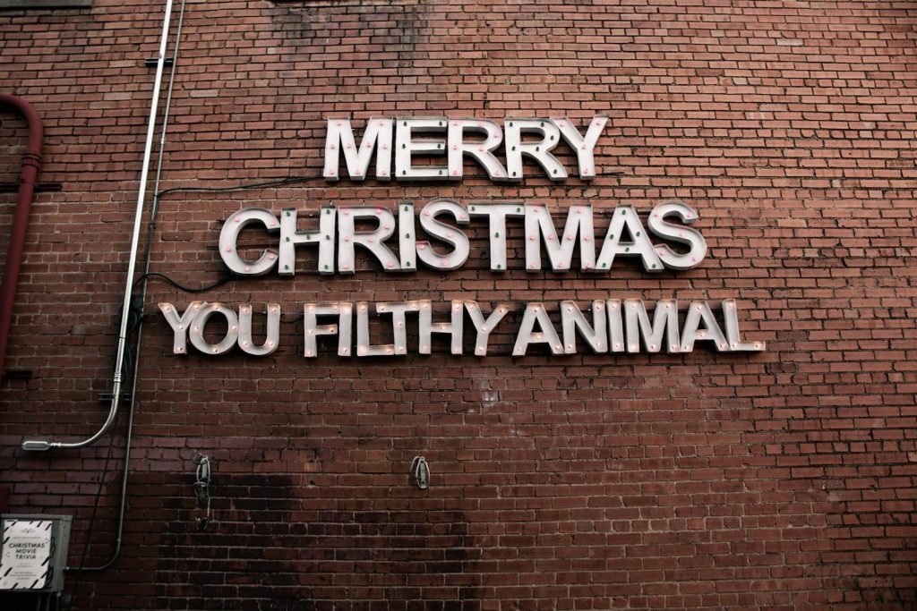 Brick wall with festive 'Merry Christmas You Filthy Animal' sign.