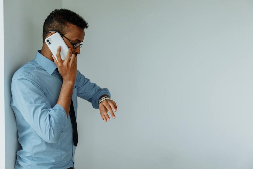 Professional man in office attire checking time on wristwatch while on phone call indoors.
