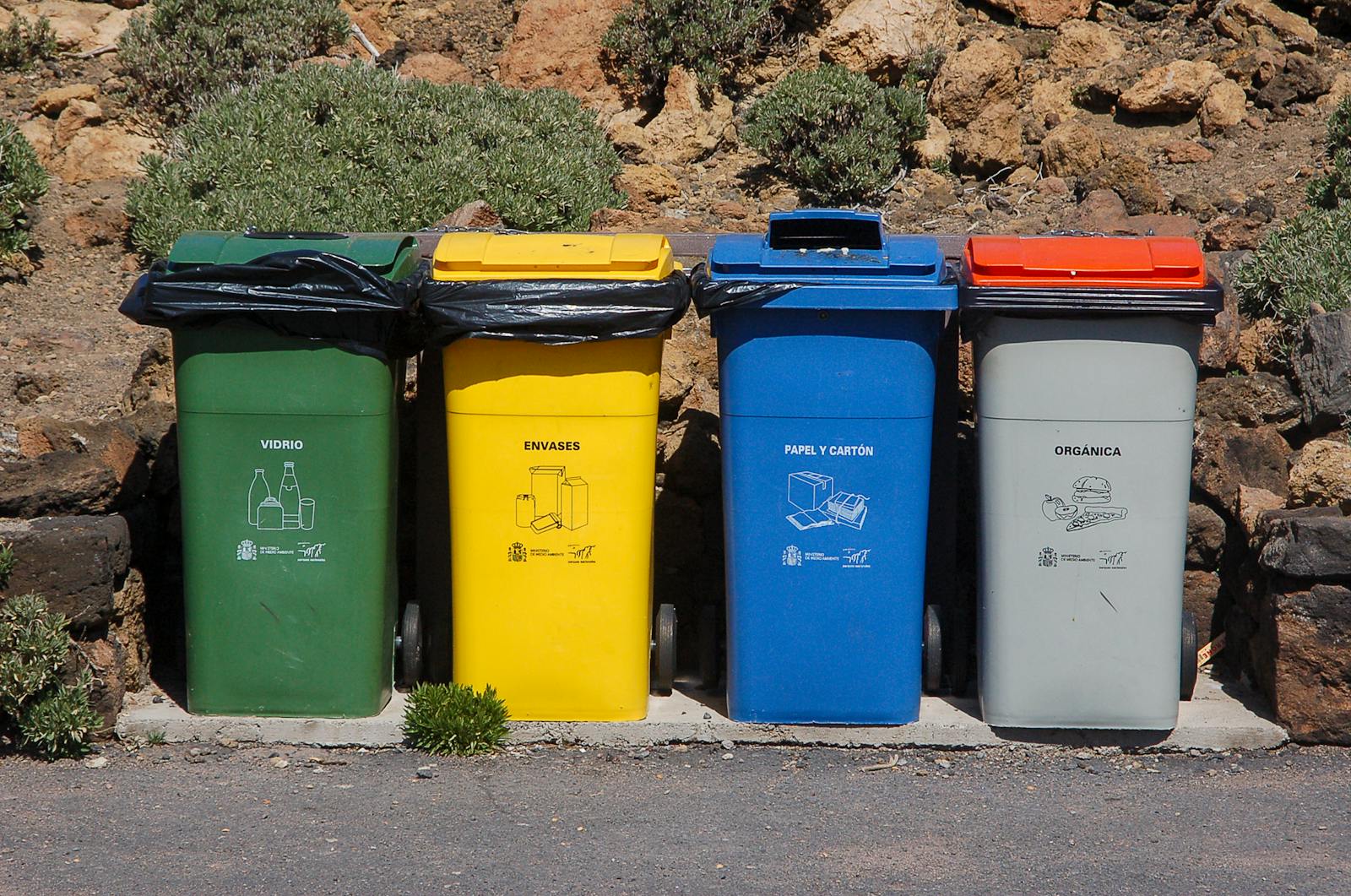 Four recycling bins for glass, packaging, paper, and organic waste outdoors.