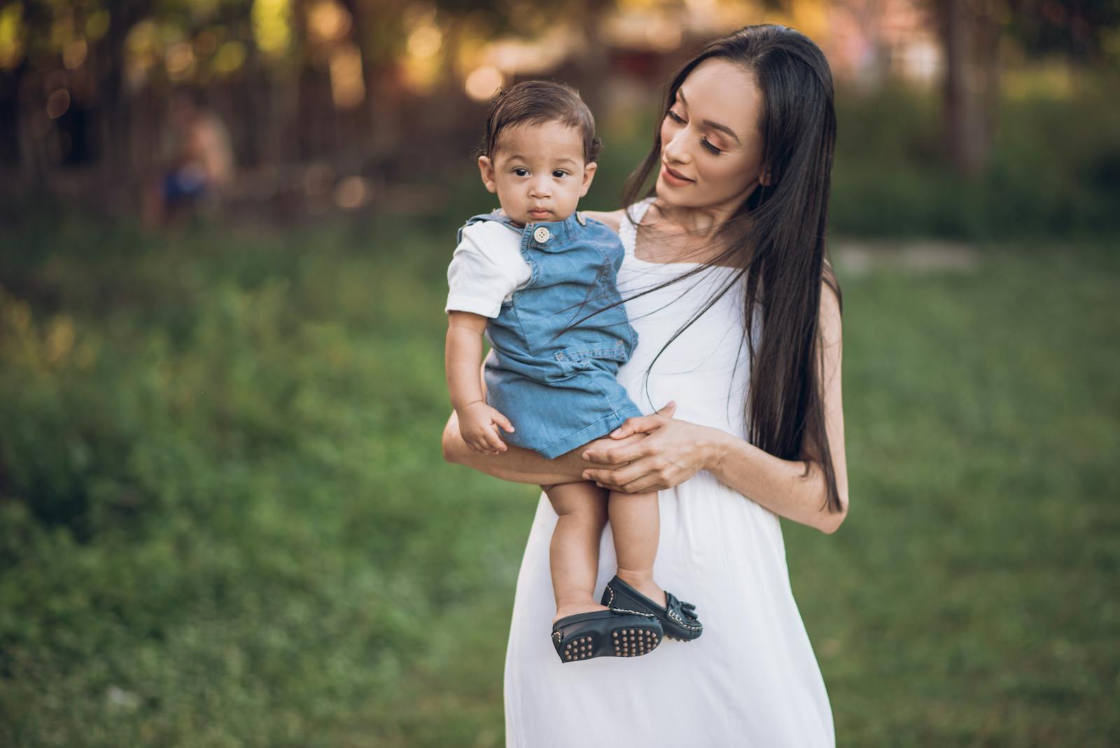A mother holding her baby in a sunny park, enjoying quality family time outdoors.