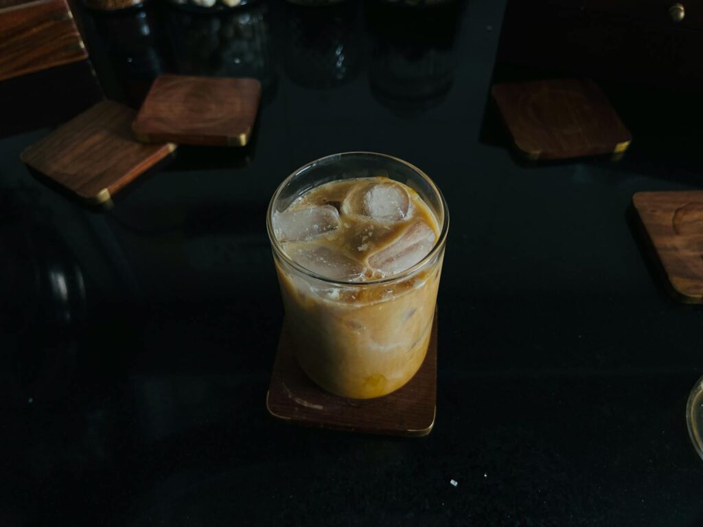 A glass of iced coffee on a wooden coaster, perfect for a refreshing break.