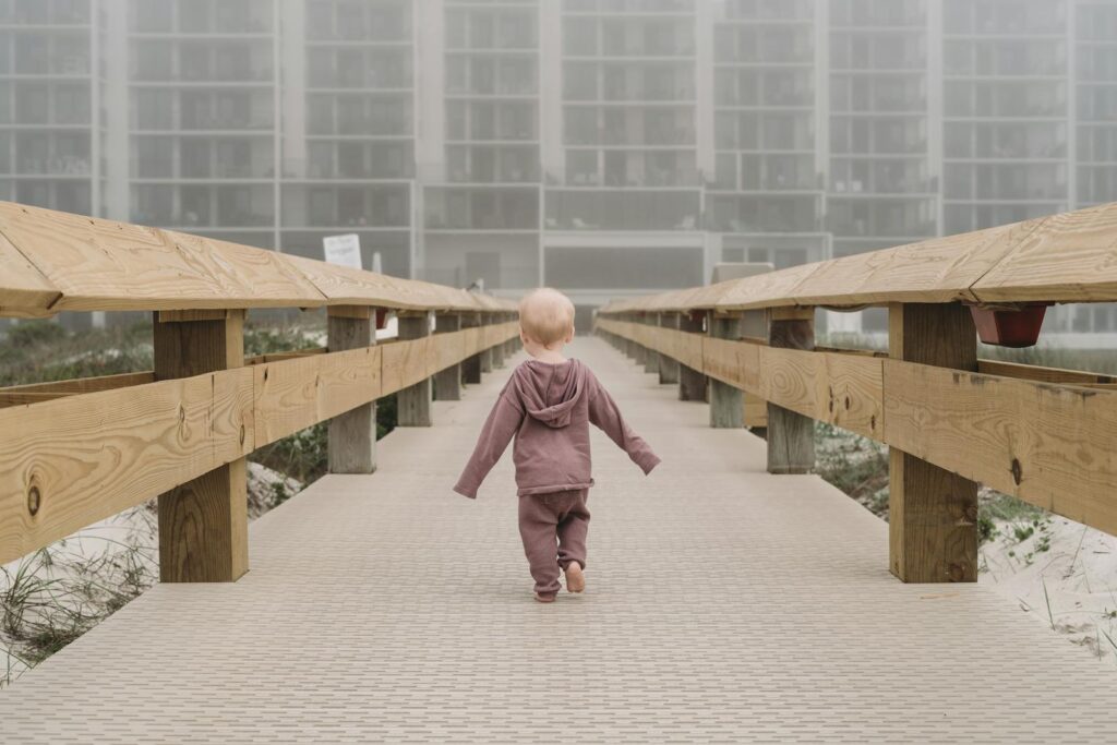 A young child in a hoodie walks on a foggy boardwalk in Orange Beach, AL.