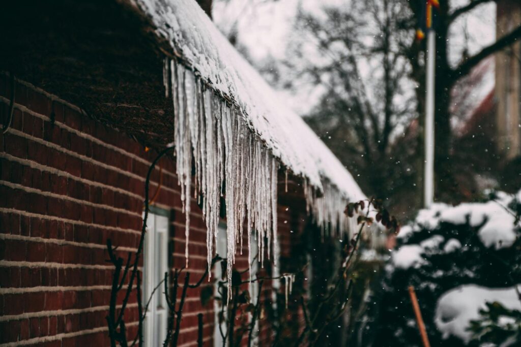 Icicles hang from a snowy brick house roof during winter, capturing cold ambiance.