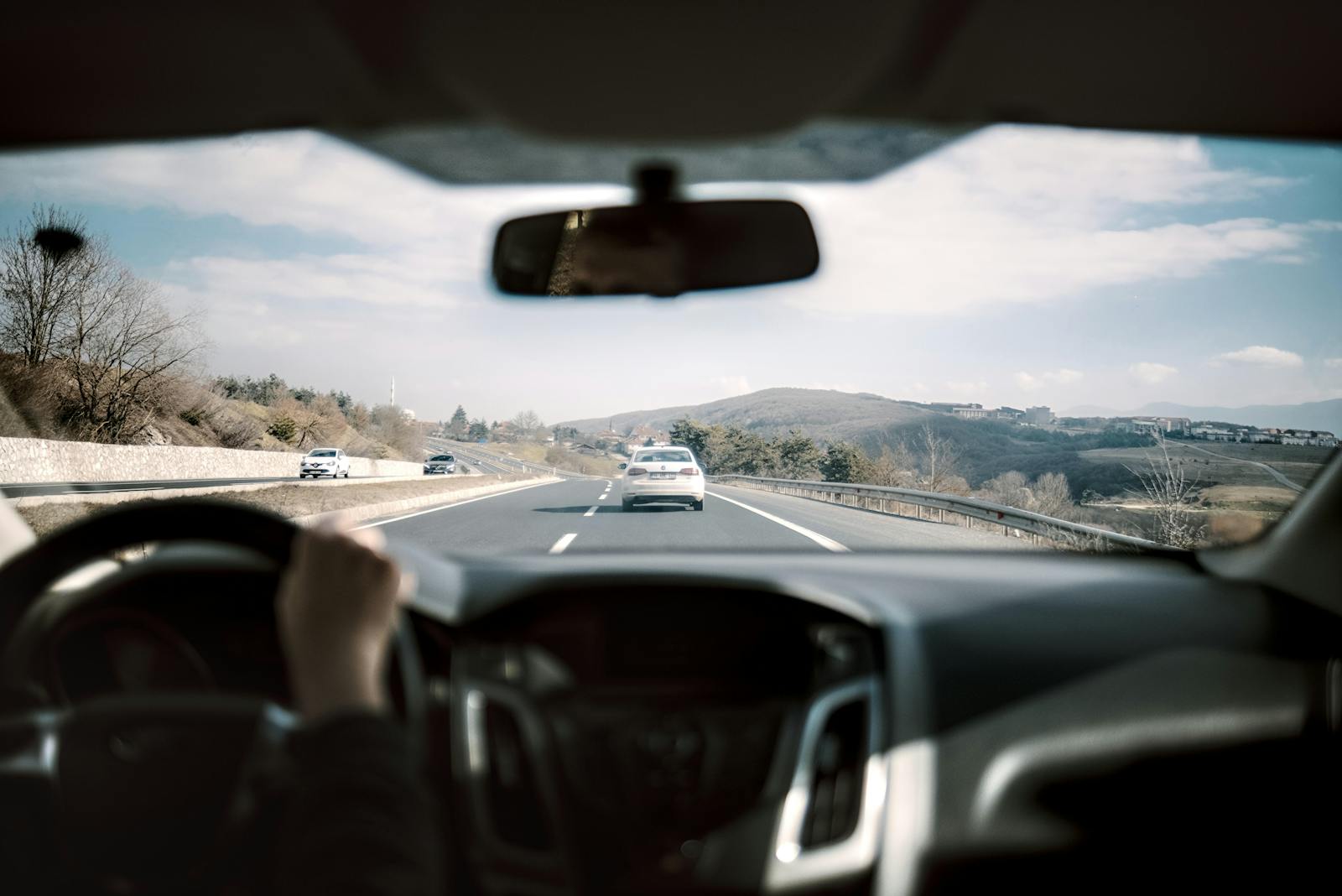 View from a car driving down a scenic highway with hills in the background, depicting a casual road trip.