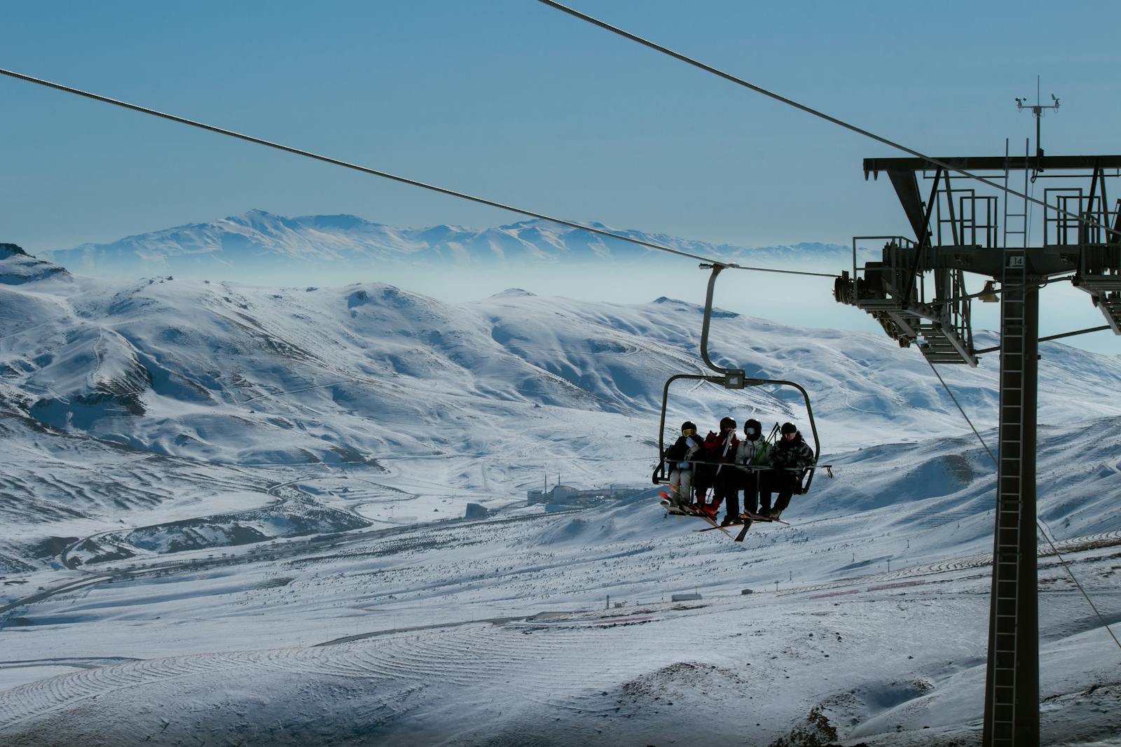 Ski lift carrying skiers over a snowy mountain landscape on a clear winter day.