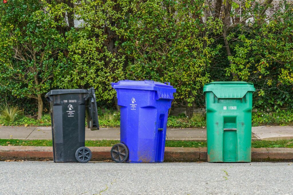 Black, blue, and green recycling bins on the street curb, ready for collection.
