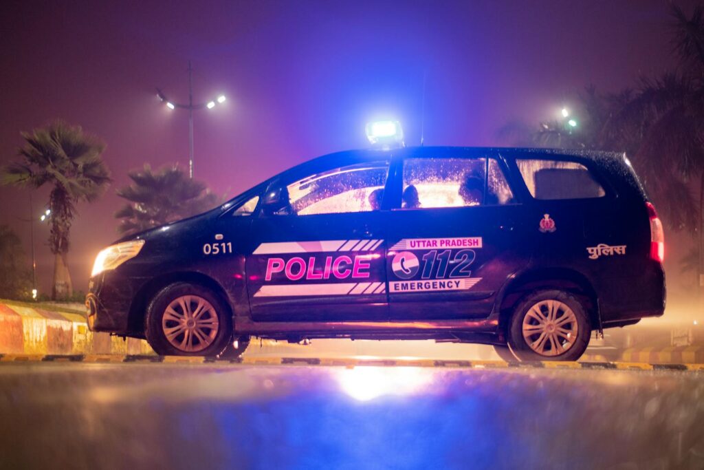 Side view of Uttar Pradesh police car parked at night, illuminated by neon lights and street lamps.