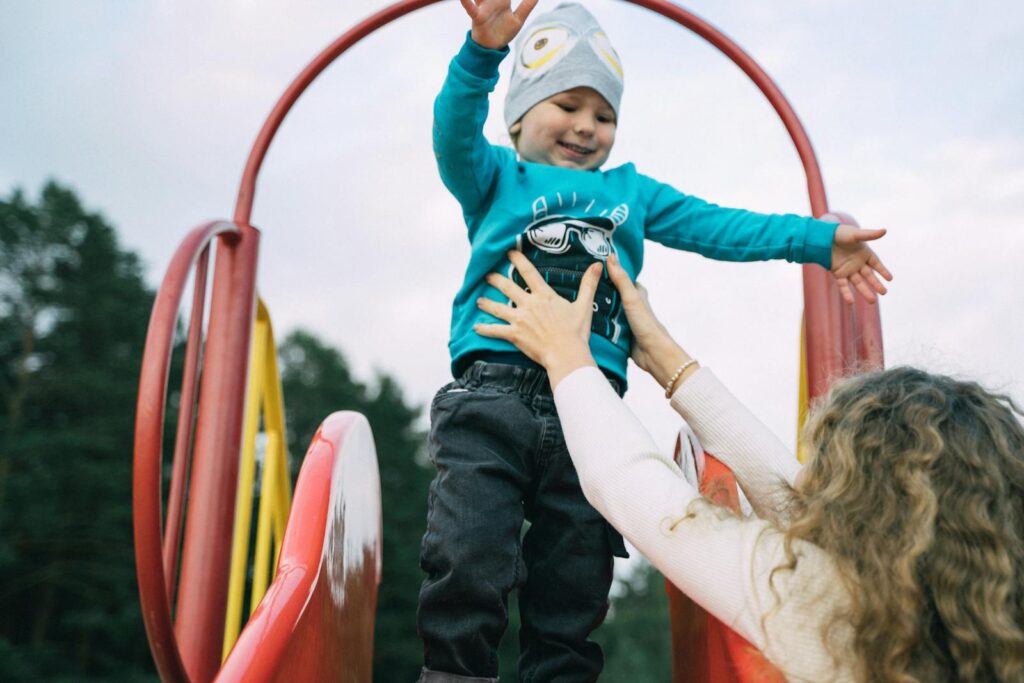 A joyful moment of a mother catching her child at the top of a playground slide.