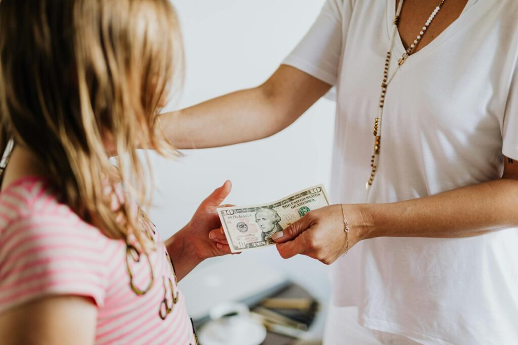 A woman handing money to a young girl, symbolizing family financial education and transactions.