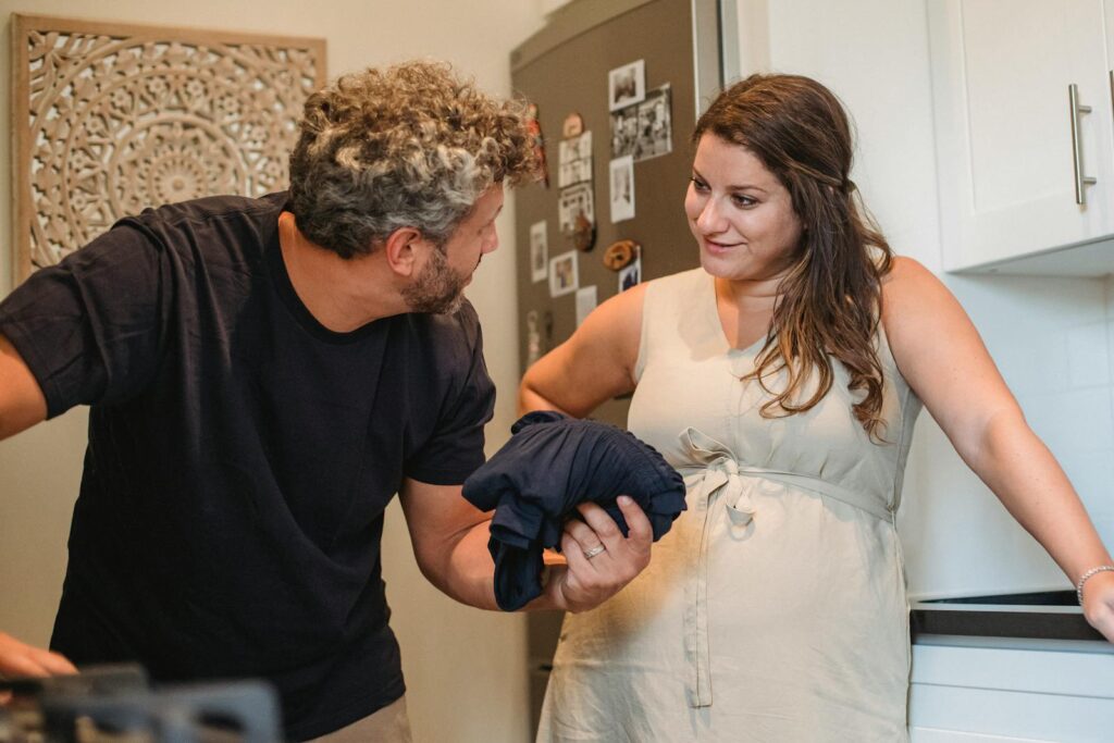 Young pregnant woman having conversation about laundry with bearded male standing kitchen