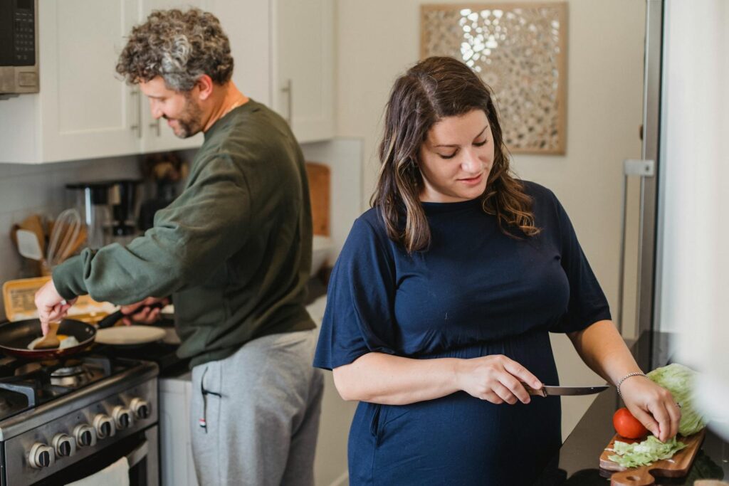 A pregnant woman and her partner cooking a healthy meal together in their kitchen.