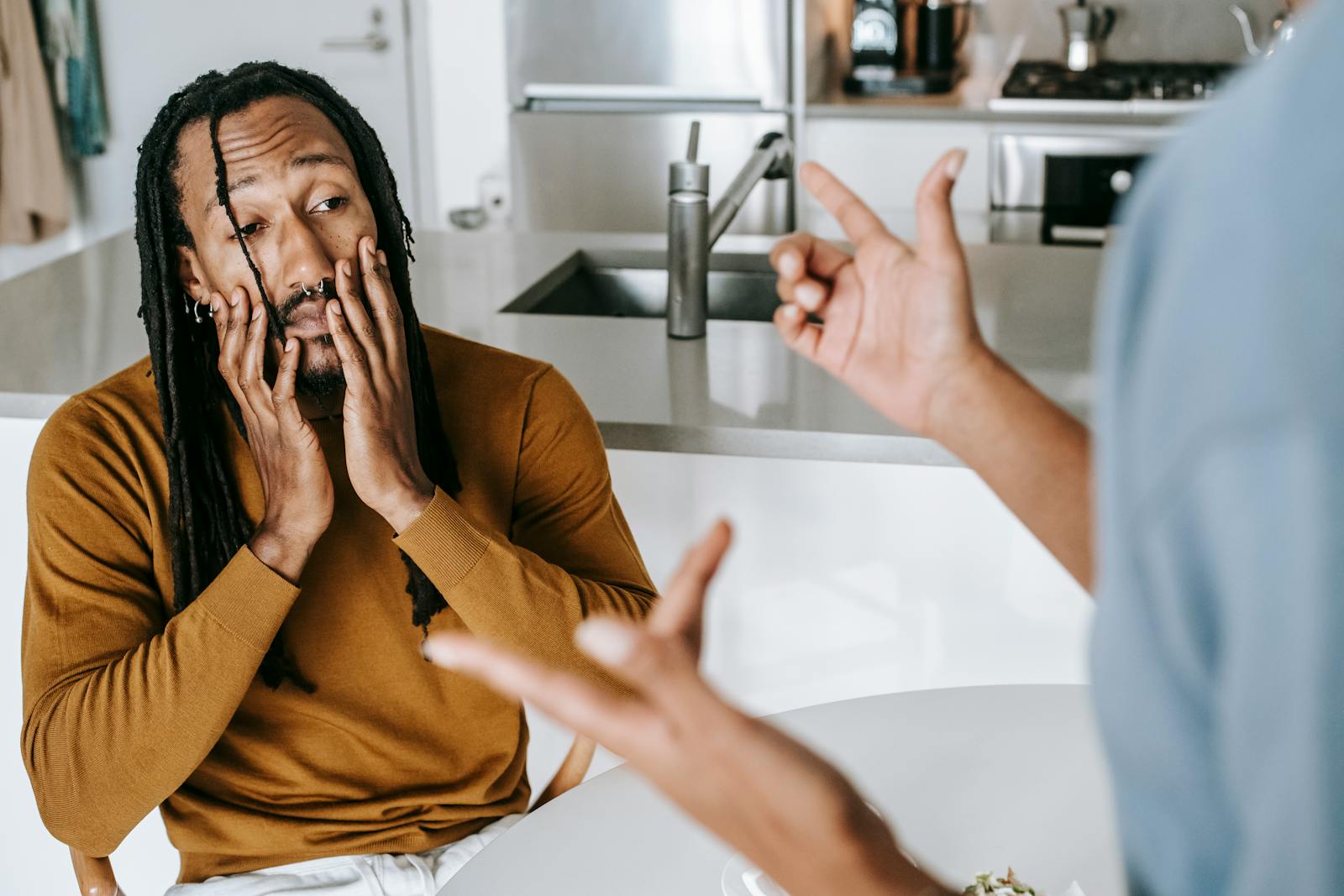Young African American male sitting at table with hands on face and having conflict with female on kitchen