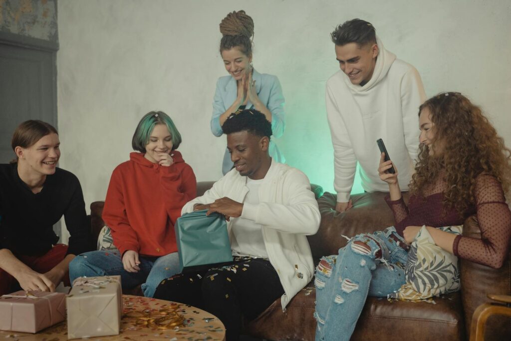 A group of friends celebrating a birthday opening presents indoors, showcasing diversity and camaraderie.