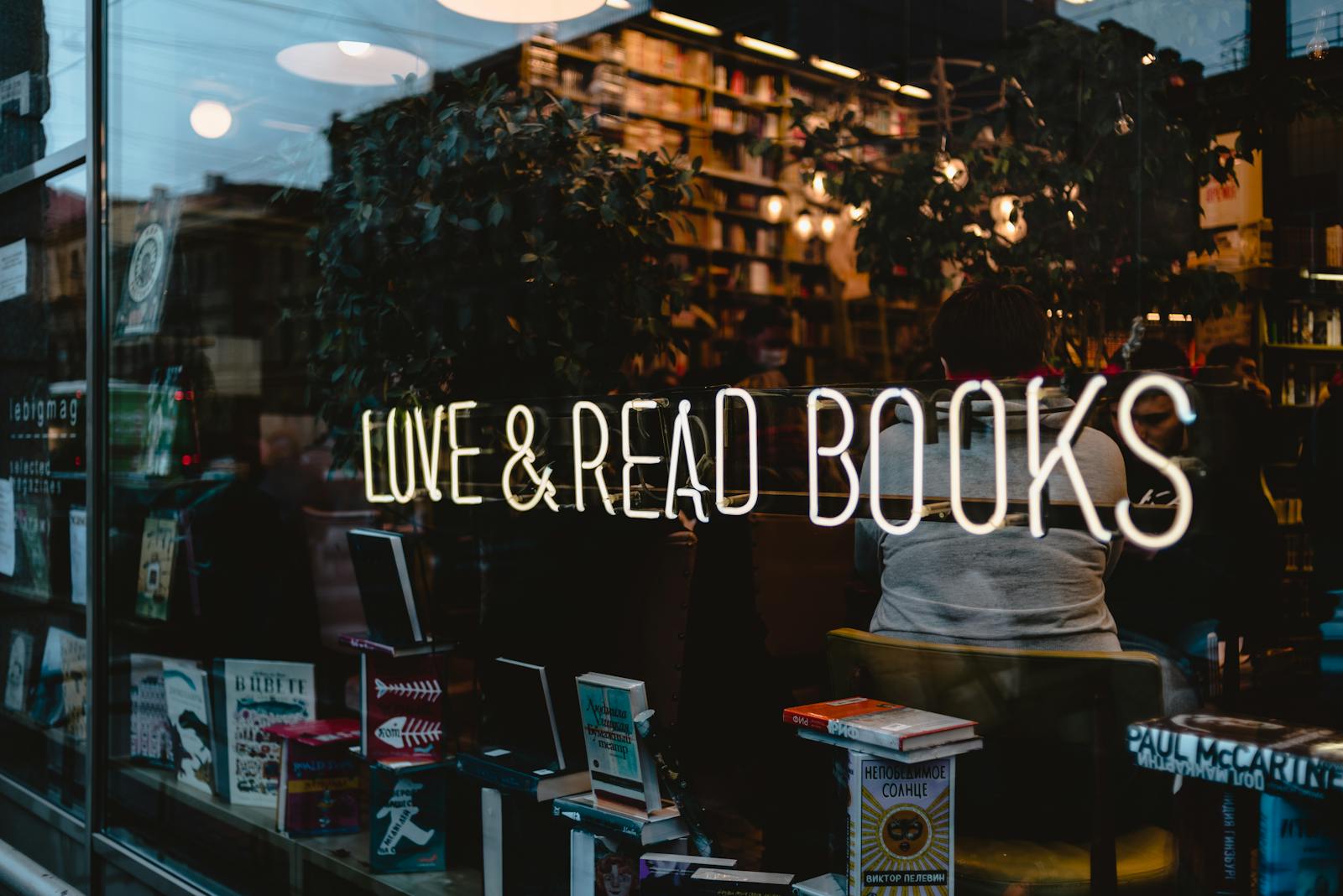 Warm bookstore interior with neon 'Love & Read Books' sign reflected in the window.