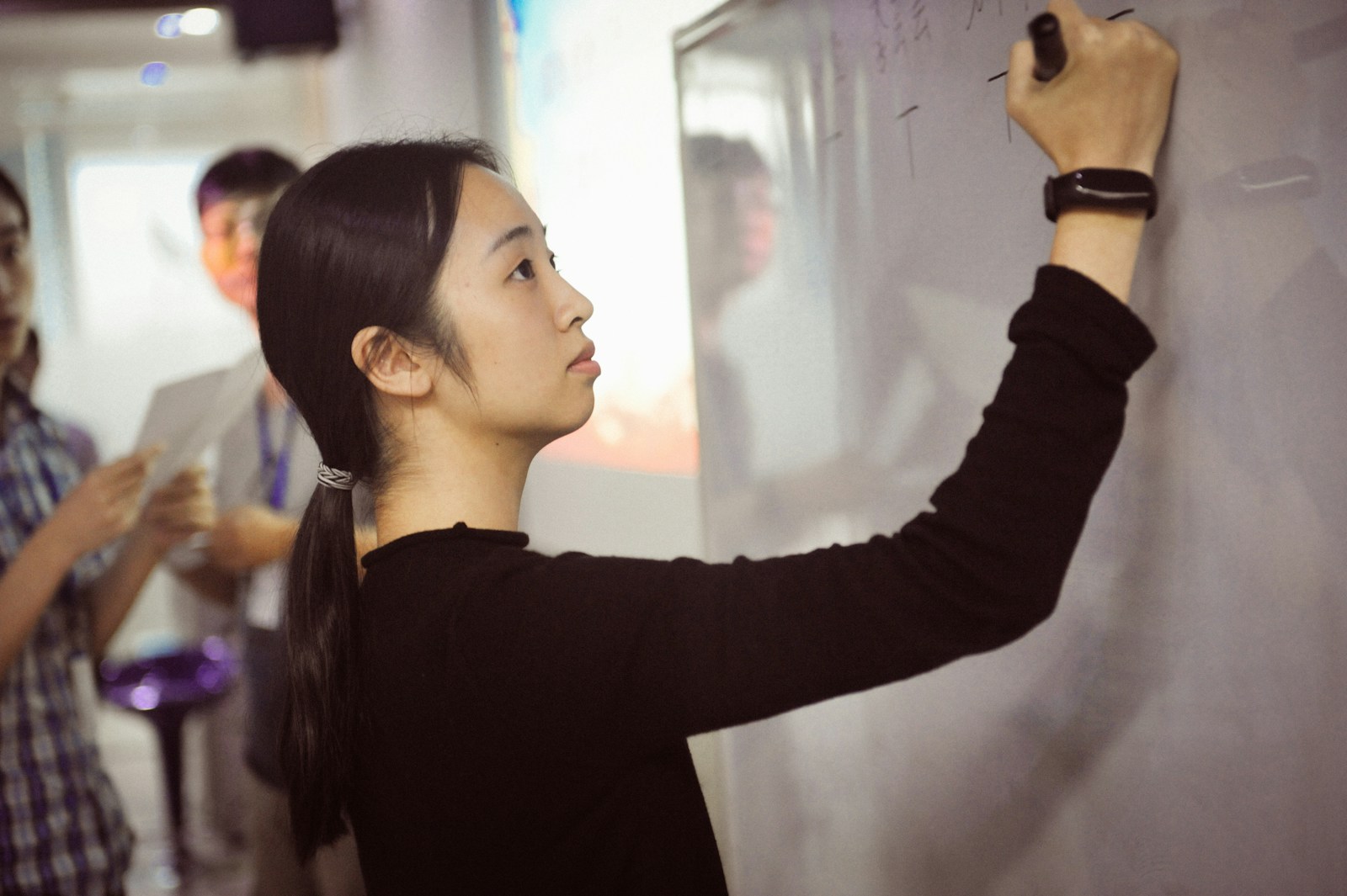 A young woman writes on a whiteboard.