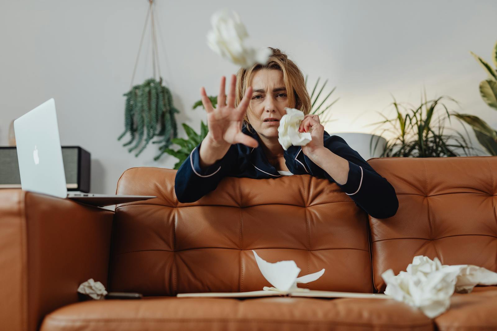 A woman in pajamas throws crumpled papers on a couch, relaxing indoors.