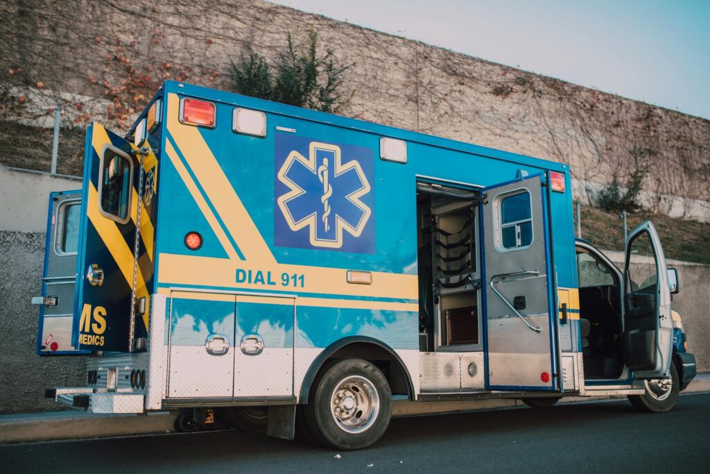 Blue ambulance parked on roadside with open doors, emergency medical service vehicle.