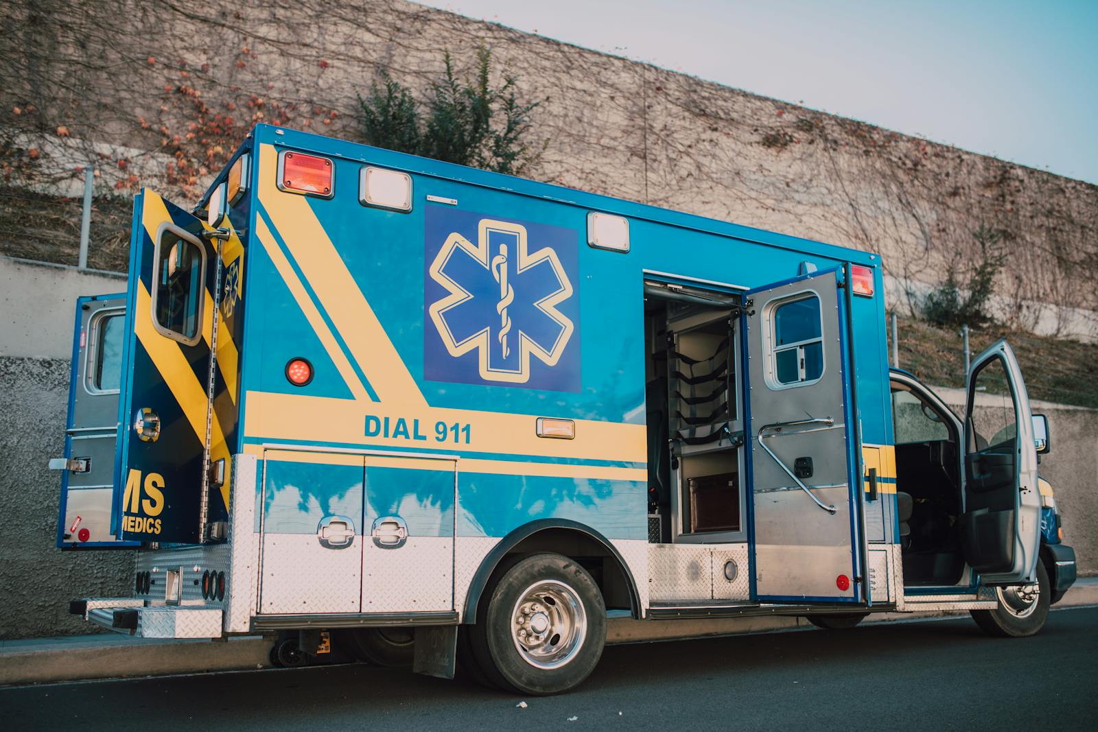 Blue ambulance parked on roadside with open doors, emergency medical service vehicle.
