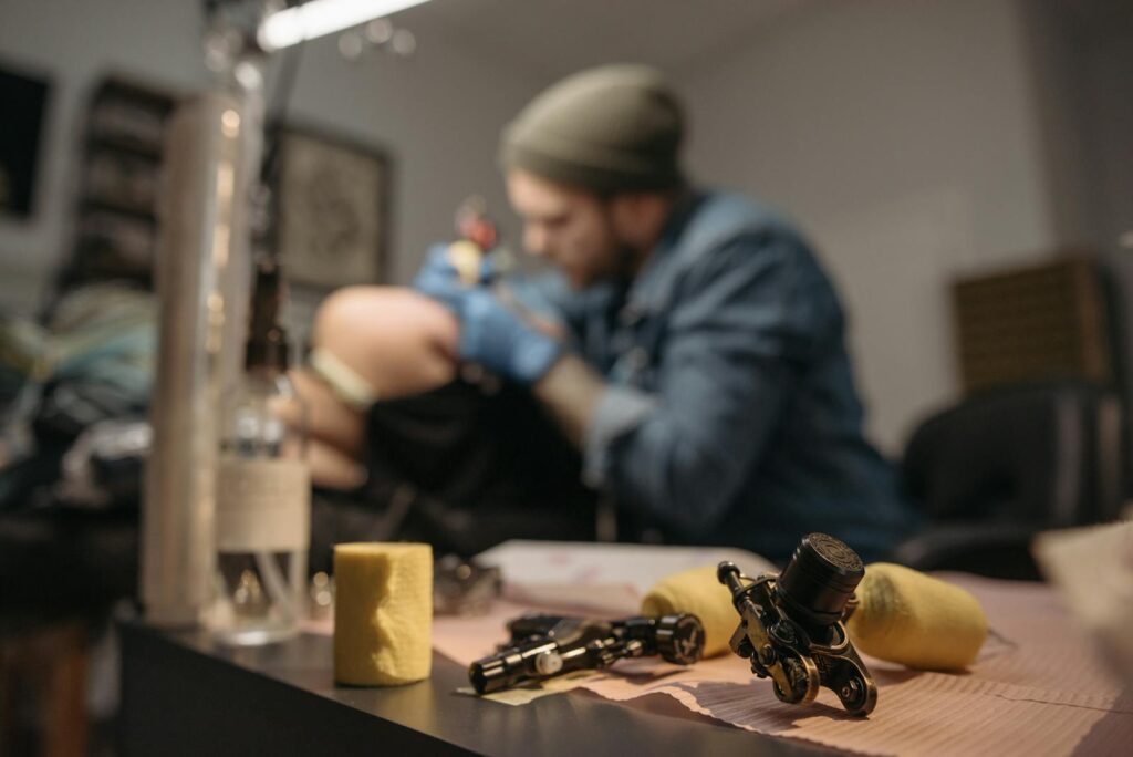Focused tattoo artist creating art in a modern parlor with equipment in the foreground.