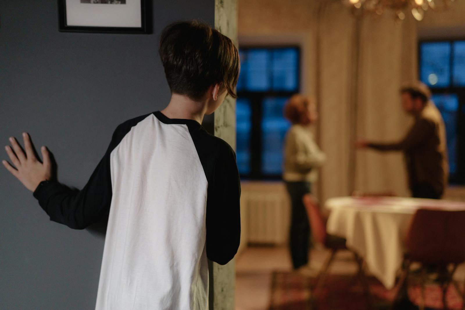 A child watches parents arguing from a doorway in a cozy home setting.
