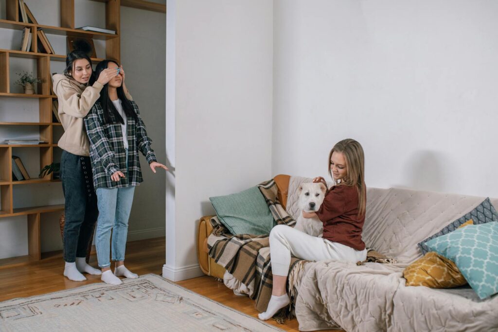 Three women share a joyful moment with a surprise gift—a cute dog, creating a heartwarming scene.