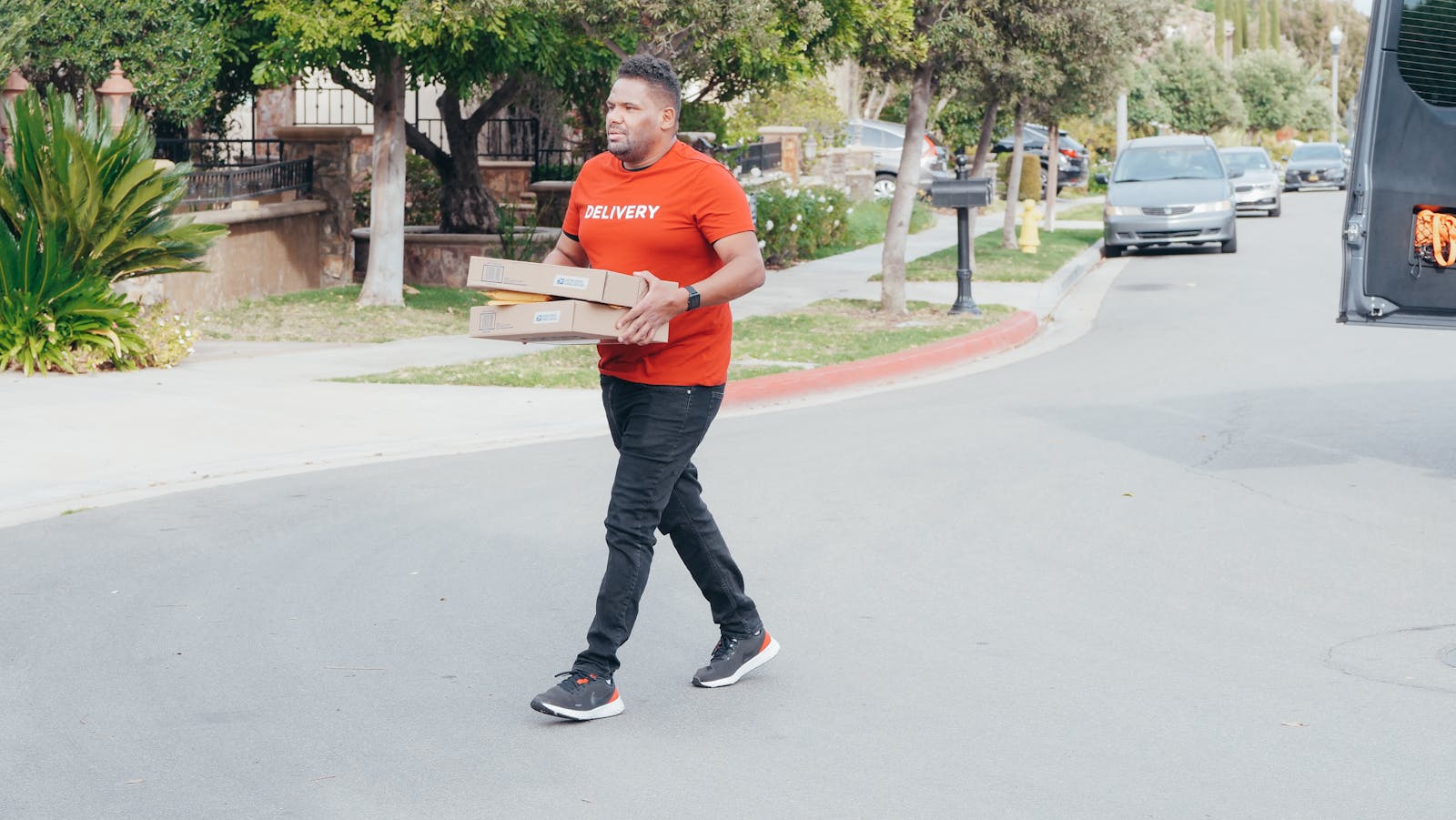 Delivery person carrying packages in a suburban neighborhood street during the day.