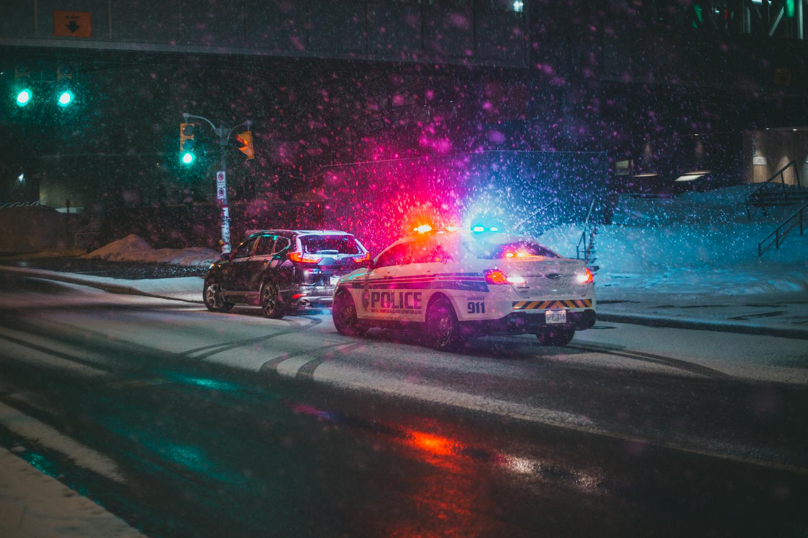 Police car with flashing lights during a snowy night on a city road.