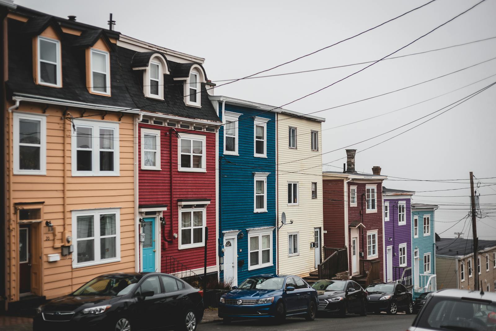 Vividly painted row houses lining a steep street with parked cars and overcast sky.