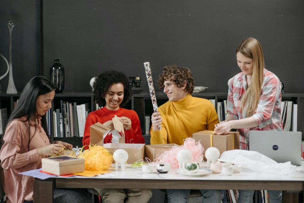 A diverse group of happy adults wrapping gifts together at a table indoors.
