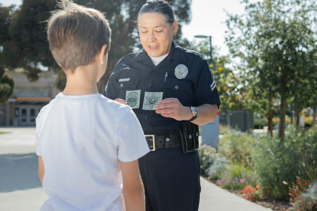 A police officer shows her badge to a child outside in a community setting, fostering trust.
