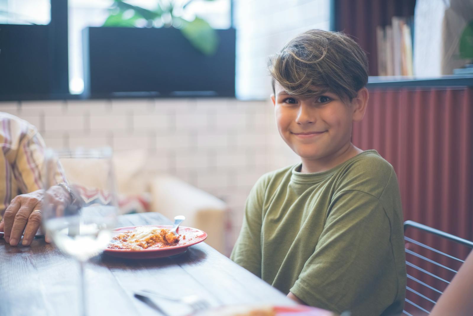 Cute child smiling at a family dining table, enjoying a meal indoors.